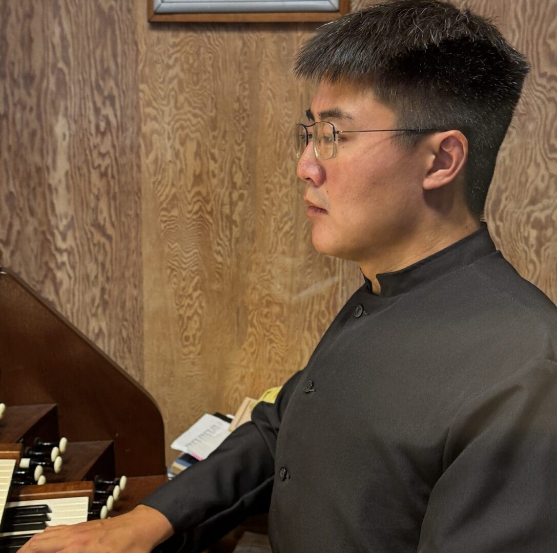 Man playing organ, wearing glasses.